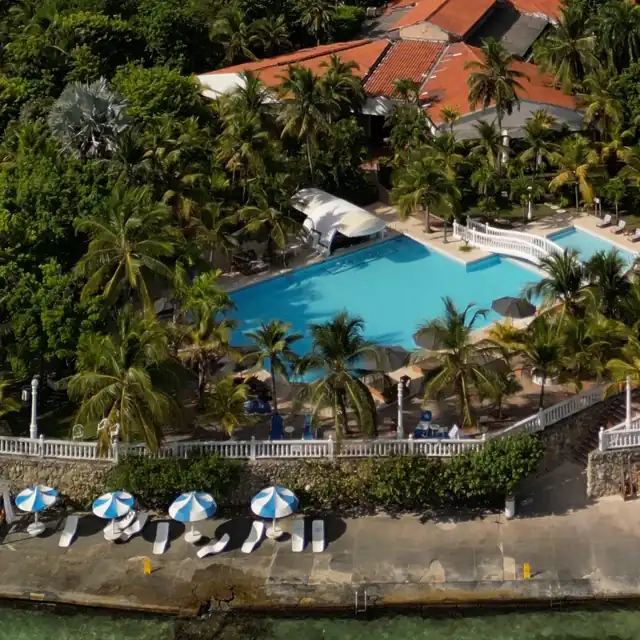 Beach club with a pool, palm trees and umbrellas by turquoise water in the Rosario Islands